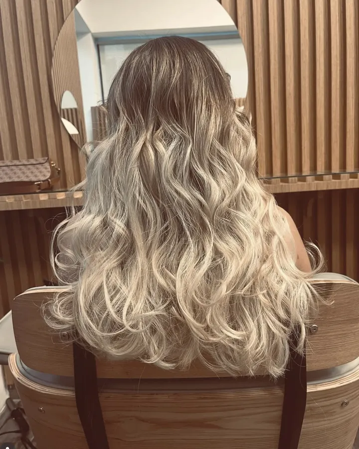 Balayage blond ondulé, vu de dos devant le miroir du salon
